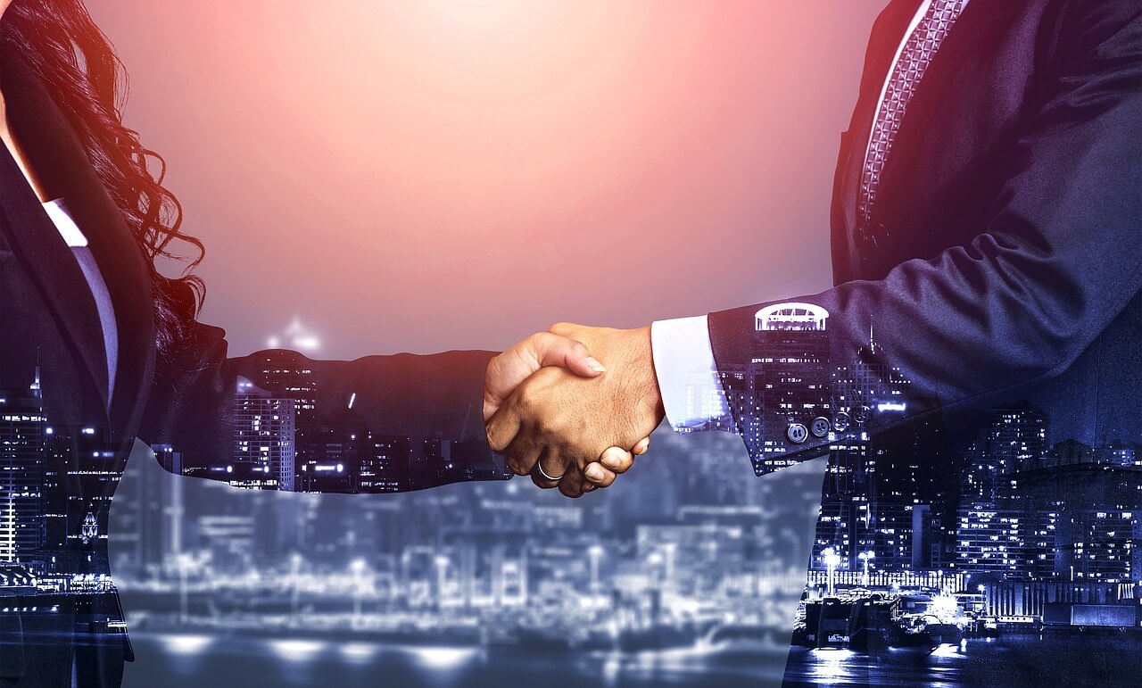 Two people shaking hands in front of a car.